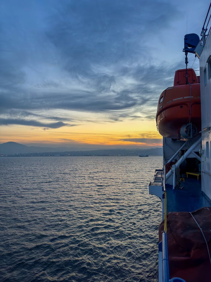 A ship sails on a tranquil sea under a vibrant sunset, creating a serene maritime scene.